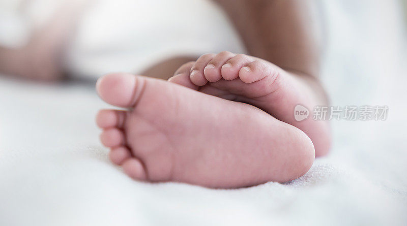Closeup feet of newborn African black baby infant isolated on white hospital bed sheet. Healthcare and medical love lifestyle father or motherâs day, nursery day care background concept banner